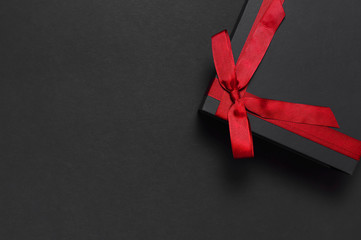 Black gift box with red ribbon on dark background top view flat lay. Holiday concept, birthday...