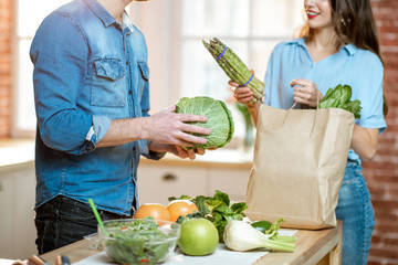 Young couple unpacking shopping back with fresh green products preparing to cook vegan meals on the kitchen at home