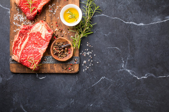 Raw Fresh Marbled Meat Beef Steak rosemary, spices  and vintage ax  on a wooden board. Black marble background. Top View Copy space for Text