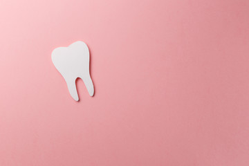 White tooth on pink background with copy space. Oral dental hygiene. Teeth whitening. Dental health concept. Oral care, teeth restoration. Dentist day concept. Flat lay. Top view. Pastel colors