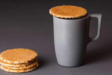 A glass cup of black tea with stack of dutch waffles on dark grey background.