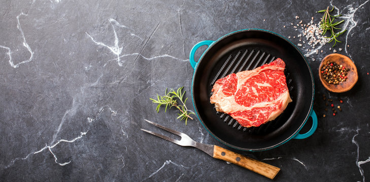 Raw Fresh Marbled Meat Beef Steak rosemary, spices on the grill pan. Black marble background. Top View Copy space for Text