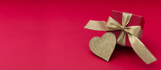 Red gift and shiny gold heart on red background, banner, view from above, copy space