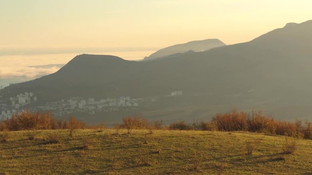 Panoramic view of the scenic autumn valley from a steep bushy slope on sunset sky background. Shot. Spectacular mountain view of a small villadge and a field in sunset golden light.