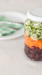Glass with grated beetroot, carrot and cucumber and a plate on background