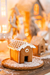 Christmas decorations and Holiday mood. Morning in the bright living room. Gingerbread house on wooden table. Defocused garland lights on background.