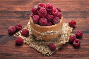 Raspberries in a wooden plate on a brown wooden board. Delicious fresh forest berries
