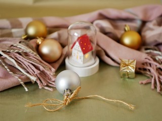White toy house with a red roof, a warm scarf, Christmas balls on a light golden background, the concept of seasonal winter holidays, home comfort