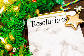 2019 New Year's Resolutions with christmas tree branches, golden star, candy cane and snowflakes on wooden background
