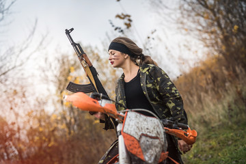 Woman soldier with rifle sitting on motorcycle