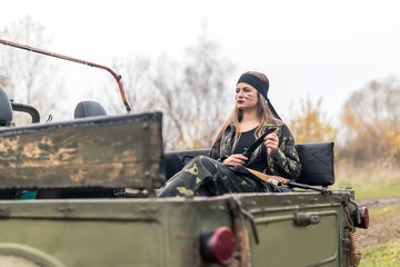 Woman soldier with rifle posing near military car