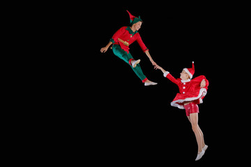 Christmas time, childhood, fairy tale. A young girl wearing a Santa's costume and boy wearing elf costume flying together