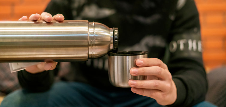 adult man pour tea and coffee in the cup from thermos at home f