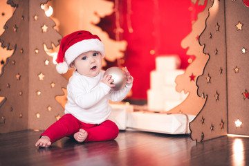 Obraz na płótnie Canvas Cute baby holding Christmas ball over lights in room. Looking at camera. Winter holidays.