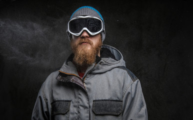 Portrait of a confident snowboarder wearing full protective equipment, isolated on a dark textured background.