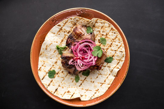 grilled meat kebab with pickled onion on pita bread on black background