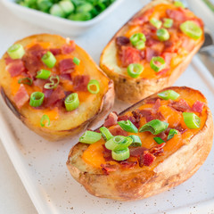 Baked loaded potato skins with cheddar cheese and bacon on ceramic plate, garnished with scallions and sour cream, square format