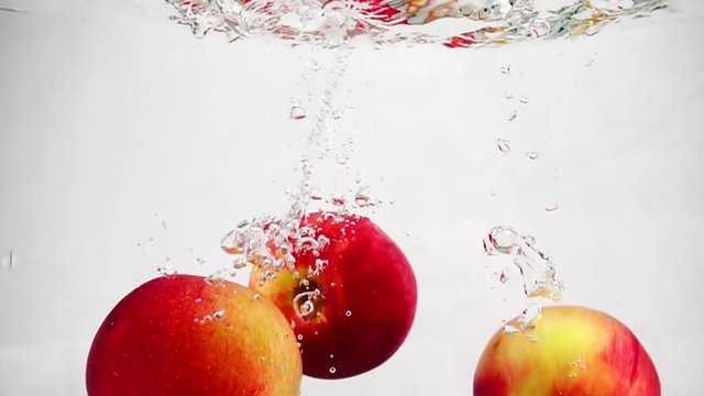 Ripe red apples fall into the water with bubbles. Video in slow motion.