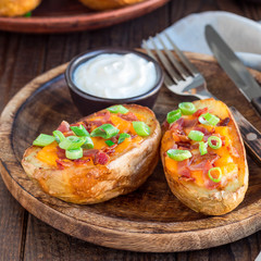Baked loaded potato skins with cheddar cheese and bacon, garnished with scallions and sour cream, square format