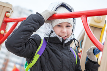 Playful young girl walking on playground at cold winter day, looking at camera and laughing © Kekyalyaynen