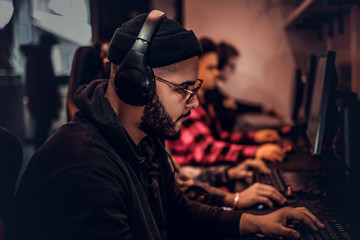 A young African American guy, enjoying spending time with his friends, playing in a multiplayer video game on a PC in a gaming club or internet cafe.