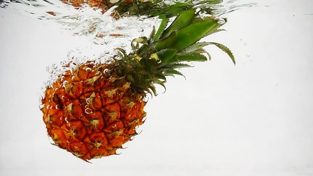 The pineapple slowly sinks into the water with waves and bubbles.