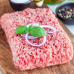 Minced meat from pork and beef. Ground meat with ingredients for cooking on a wooden board, square format