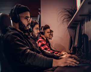 A young African American guy, enjoying spending time with his friends, playing in a multiplayer video game on a PC in a gaming club or internet cafe.