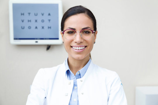 Pretty young woman ophthalmologist smiling while looking at camera in the consultation.