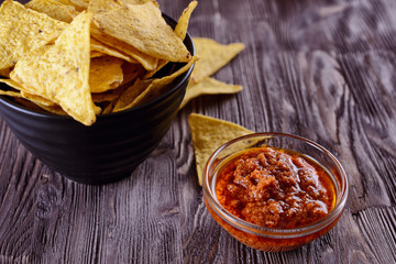 Nachos, corn chips in a black bowl and tomato salsa or pesto  on a wooden background