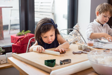 Little girl rolling gingerbread dough for Christmas cookies . Lifestyle image, natural light, bokeh.