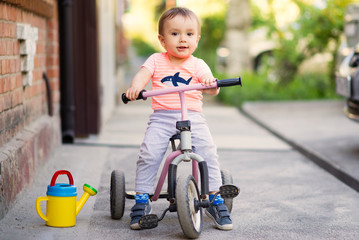 Portrait of a little child on a three wheel bike (tricycle) on a tarmac pavement in a warm sunny...