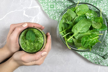 Top view on female hands holding a cup with green healthy (kiwi and spinach) smoothie and a glass bowl filled with spinach on a piece of fabric. Concept of healthy eating/ dieting. 