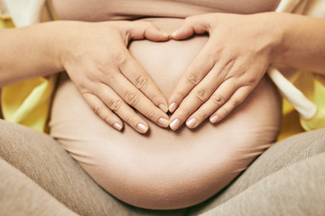 Pregnant woman making heart shape with hands on belly. 