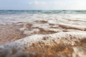 Low angle, camera on the ground, lens covered with water drops to emphasise wetness - close up of shallow sea waves washing beach sand. Abstract marine background.