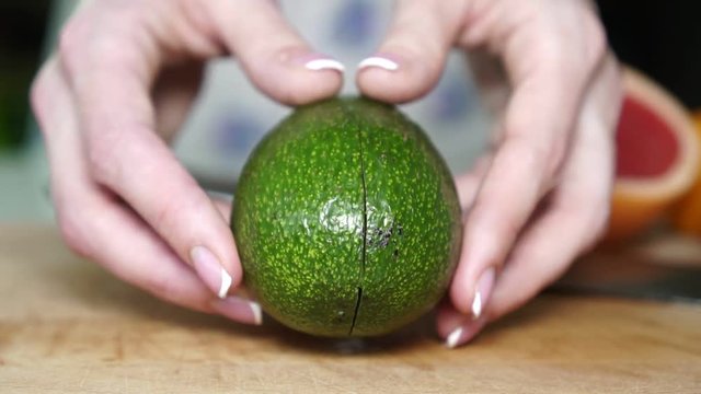 Woman cuts green avocado in half.