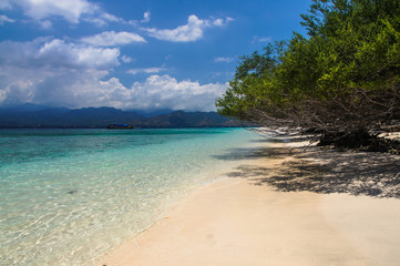 Sandy beach with blue water on the tropical island of Gili Meno. The mountains of Lombok on the horizon.