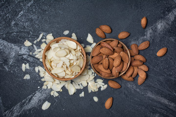 Top view of almond slices and whole nut on black marble background