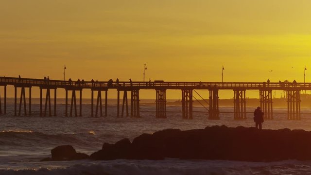 Silhouette of pier at sunset with waves in slow motion