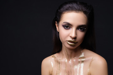 Fashion young clean skin Woman face portrait close up on black background. Model girl with holiday golden Glamour shiny professional makeup. Beauty gold metallic 