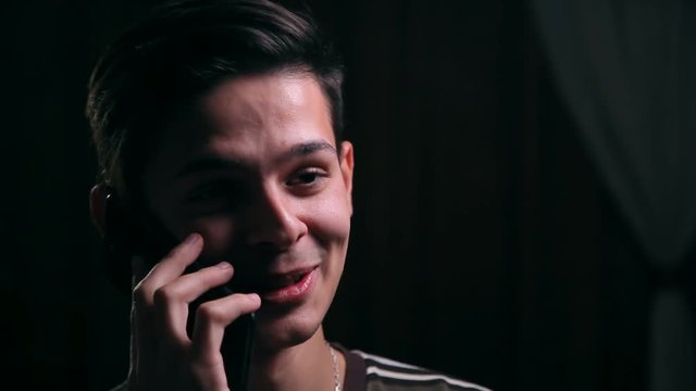 young smiley man talking on the phone in the dark room, close up