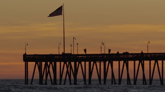 American flag flying in slow motion on pier at sunset