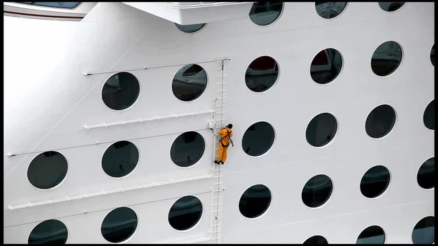 Maintenance worker repares and paints exterior of a ship at the dock