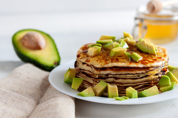 On the table there is a dish with pancakes, honey and avocado