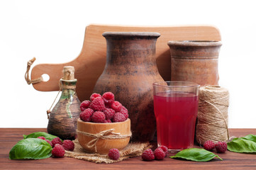 Old dishes, raspberries in a wooden bowl, and a glass of compote on a brown wooden board. White...