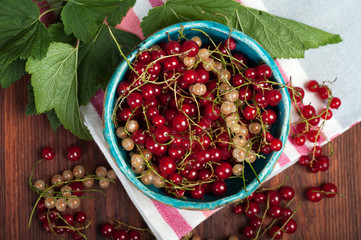 Red and white currants in a ceramic bowl on a brown wooden board. Season gathering berries.