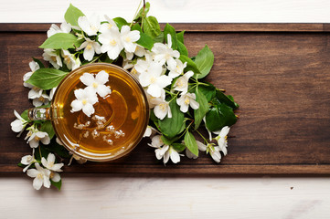 Green tea with jasmine in a glass cup on a brown wooden board. Next to the flowers are jasmine....