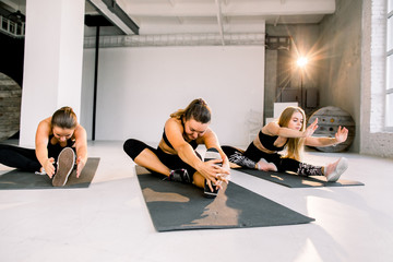 Fitness class and instructor stretching legs in bright exercise room