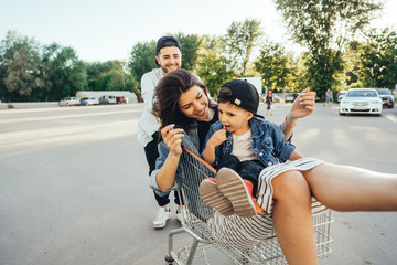 Young dad carries mom and son in a cart on the parking lot