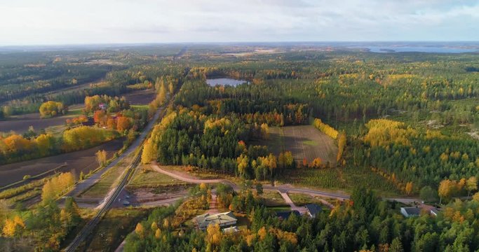 Autumn color countryside, C4K aerial, drone shot, towards forest, road, railway and a pond, on the countryside, on a sunny, fall day, in Uusimaa, Finland